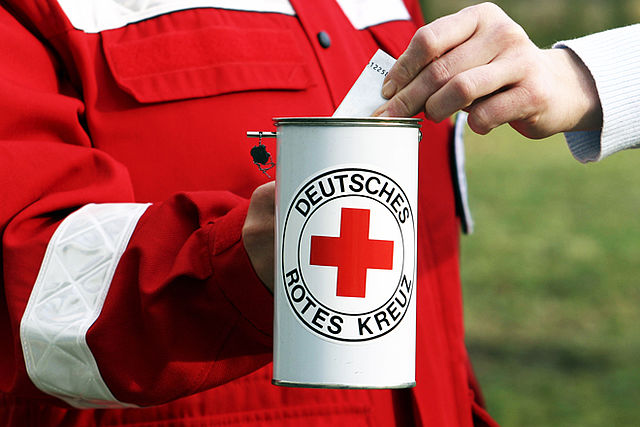 "Nahaufnahme einer Spendensammlung des DRK Eisenach: Eine Person in roter Dienstkleidung hält eine weiße Sammeldose mit dem Logo des Deutschen Roten Kreuzes, während ein Spender einen Geldschein einsteckt."