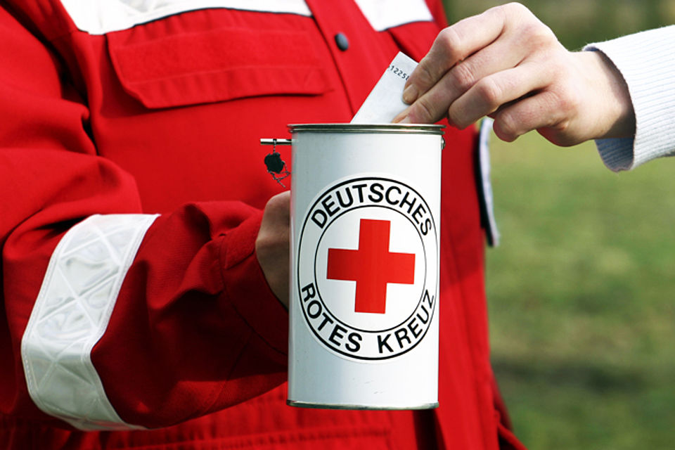 "Nahaufnahme einer Spendensammlung des DRK Eisenach: Eine Person in roter Dienstkleidung hält eine weiße Sammeldose mit dem Logo des Deutschen Roten Kreuzes, während ein Spender einen Geldschein einsteckt."