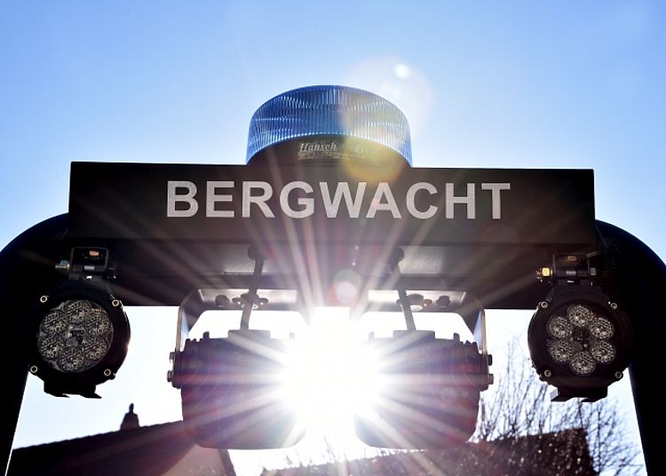Nahaufnahme der Aufschrift BERGWACHT auf dem Einsatzfahrzeug-Dach. Ein blaues Hänsch-Rundumlicht und Arbeitsscheinwerfer sind im Gegenlicht der tief stehenden Sonne sichtbar.