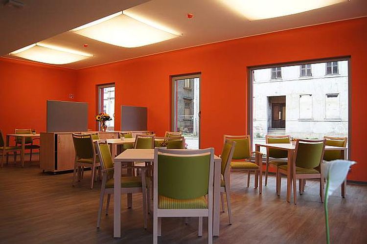 Heller Gemeinschaftsbereich im DRK Pflegeheim Haus Fischerstadt, gestaltet in leuchtendem Orange und hellgrünen Stühlen.