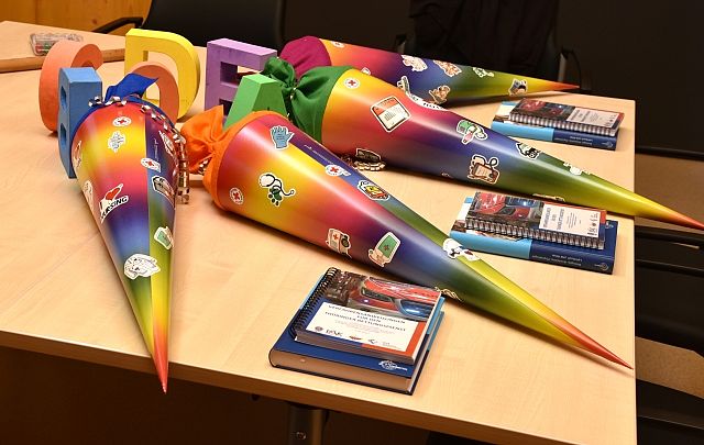 Vier bunte Schultüten mit Regenbogenfarben und verschiedenen Aufklebern liegen auf einem hellen Tisch bereit. Neben den Schultüten sind blaue Notizblöcke und große, bunte Holzbuchstaben platziert. Die Schultüten sind als Willkommensgeschenk für die neuen Auszubildenden im Rettungsdienst gedacht und stehen symbolisch für den Beginn ihrer Ausbildung.
