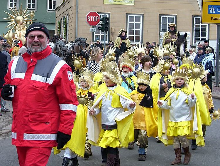 Ein ehrenamtlicher Helfer der DRK-Bereitschaft Eisenach begleitet lächelnd den Sommergewinnsumzug, während Kinder in traditionellen Sonnenkostümen vorbeiziehen