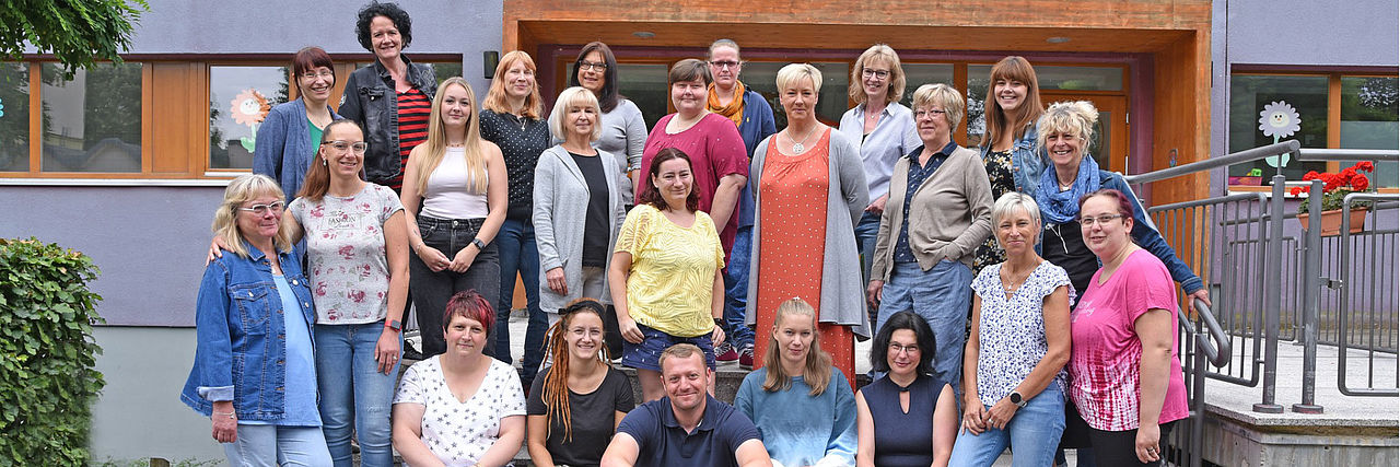 Das Team und die Leitung des DRK-Kindergartens Regenbogen auf den Stufen vor dem Kindergartengebäude.