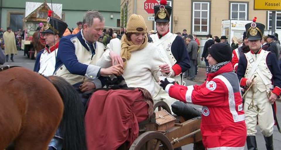 Eine Ehrenamtliche der DRK-Bereitschaft reicht während des Sommergewinns in Eisenach Getränke an Teilnehmer in historischen Kostümen auf einem Festwagen.